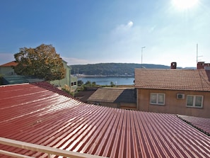 A residential area with red-tiled roofs, a body of water, and a tree in the background. - Apartments Susanne 79 (Pula)