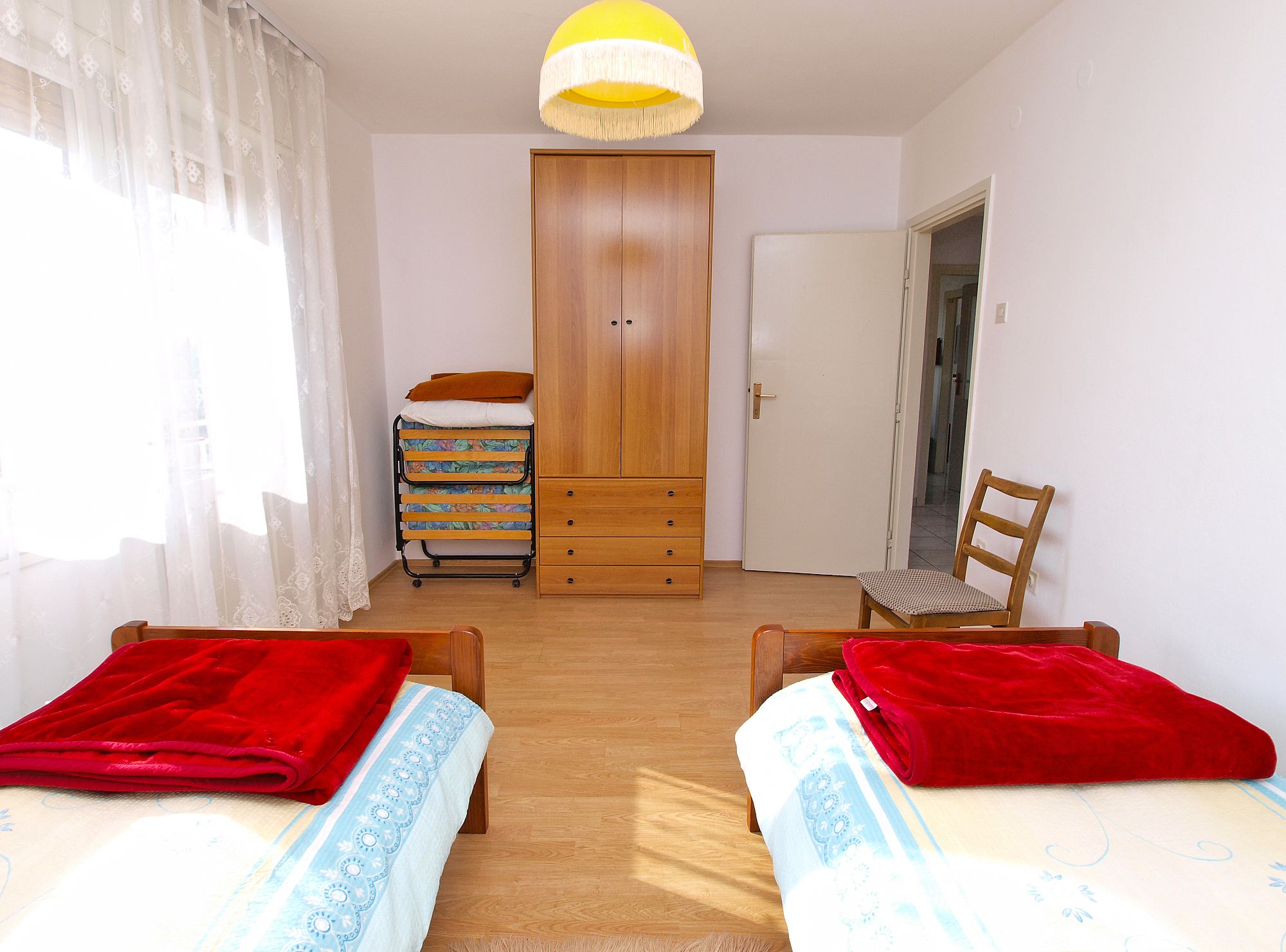 A bedroom with two beds, a wardrobe, a chair, and a small table.