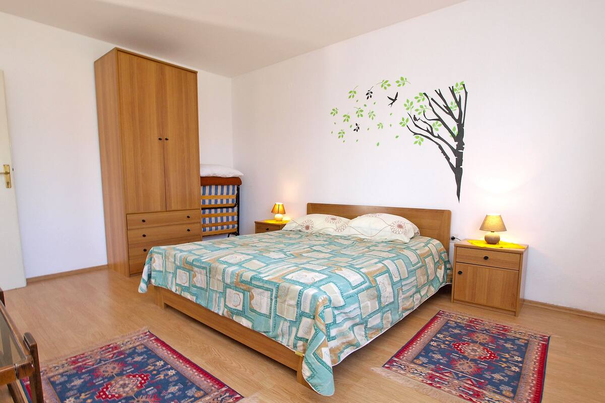 A bedroom with a bed, two bedside tables, a wardrobe, and two rugs.