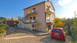 Un edificio a due piani con un balcone al secondo piano, un'auto rossa parcheggiata davanti e un cielo azzurro intenso.
