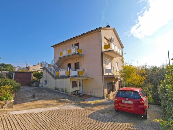 A two-story building with a balcony on the second floor, a red car parked in front, and a clear blue sky. - Apartments Susanne 79 (Pula)