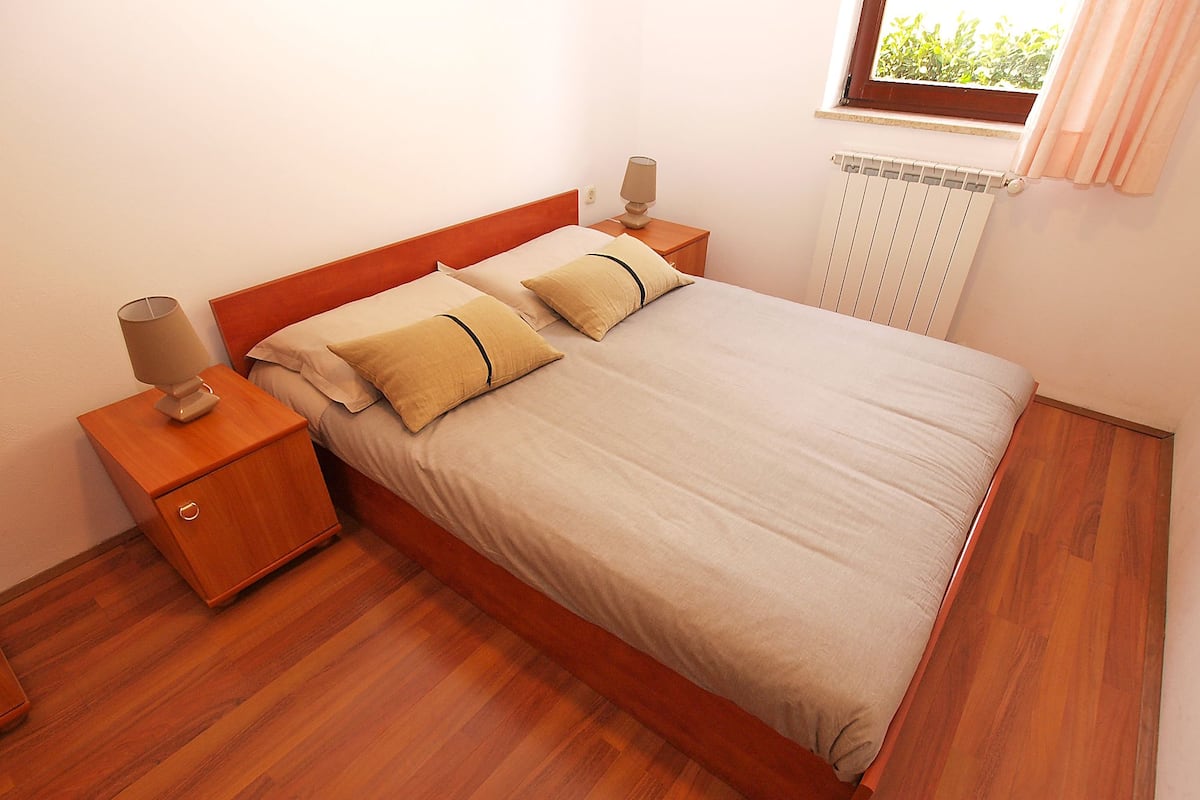 A neatly made bed with a wooden headboard, two bedside tables with lamps, and a window with curtains.