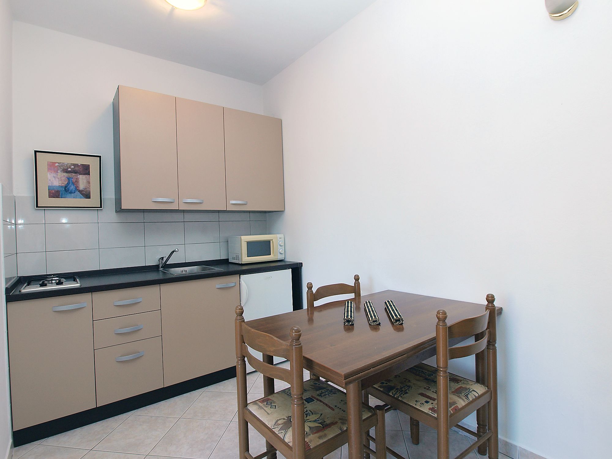 A compact kitchen with beige cabinets, a microwave, and a dining table with chairs.