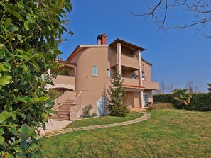 A two-story building with a stone facade, a balcony, and a small garden area.