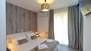 Una habitación de hotel moderna con una cama grande, un panel de madera decorativo, una lámpara de techo y una ventana con cortinas.