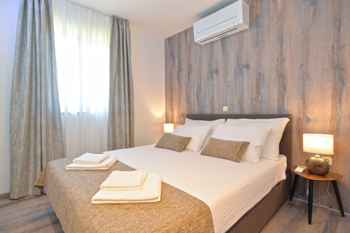 A hotel room with a large bed, wooden headboard, and a wall-mounted air conditioner.