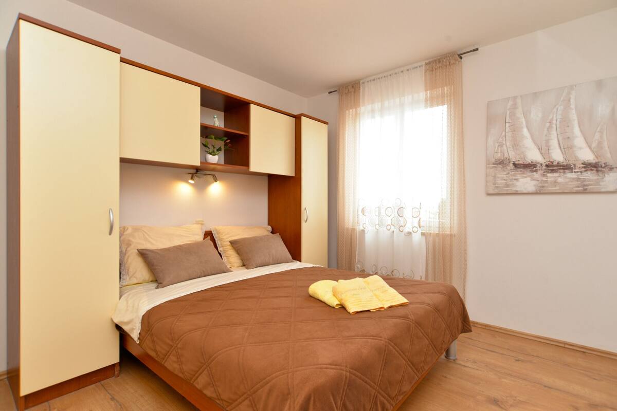 Une chambre à coucher avec un lit, une armoire, une fenêtre avec des rideaux et un tableau accroché au mur.