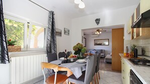Uma área de refeições com uma mesa posta para quatro pessoas, uma cozinha com fogão e uma sala de estar com sofá e ventilador de teto.