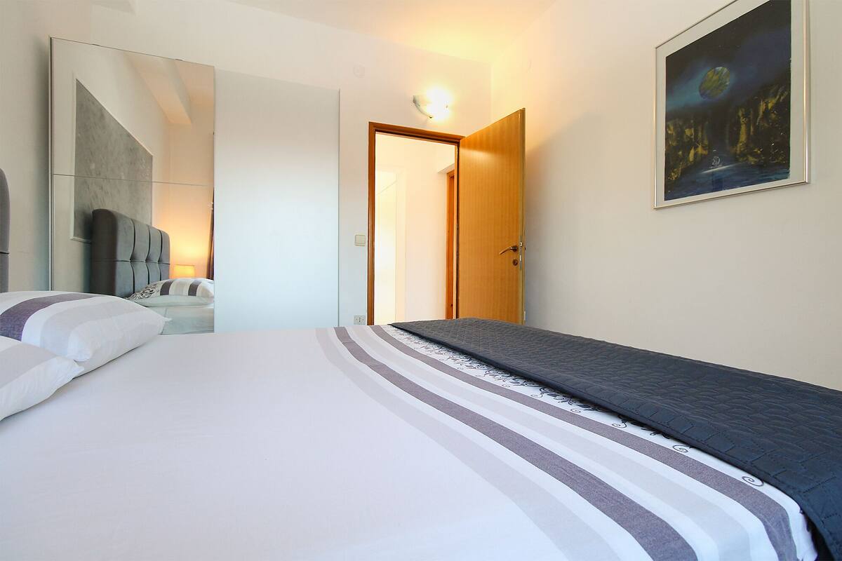 A hotel room with a bed, a large mirror, a painting, and a door leading to another room.
