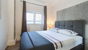 Quarto com cama, cortinas, janela, luminária e cabeceira cinza.