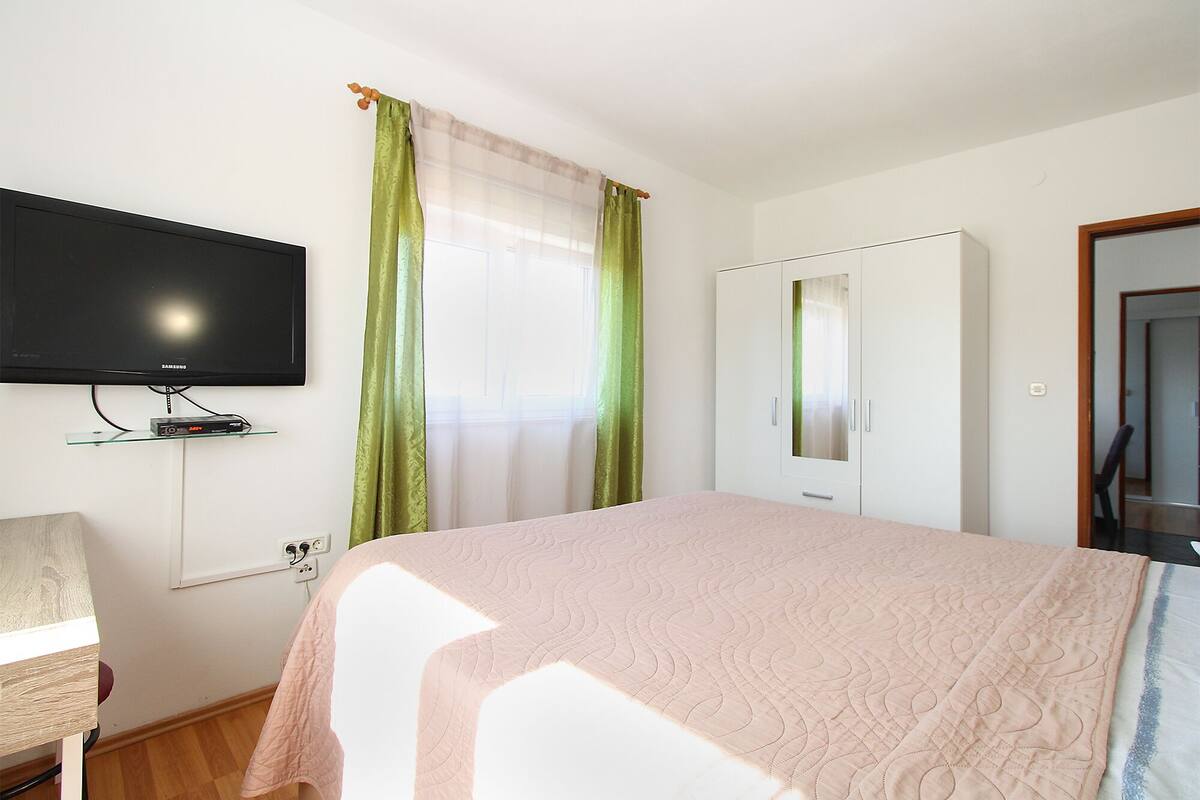 A bedroom with a bed, a television mounted on the wall, a wardrobe, and a window with curtains.