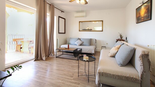 Uma sala de estar com sofá, mesa de centro, ventilador de teto e uma janela grande com cortinas.