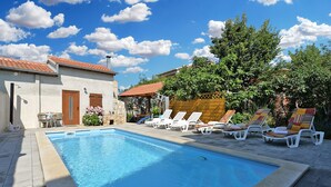 Piscina com espreguiçadeiras, um edifício de pedra e um cercado de madeira.