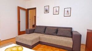 Un salon avec un canapé d’angle, un parquet en bois à motifs chevrons et trois tableaux encadrés accrochés au mur.