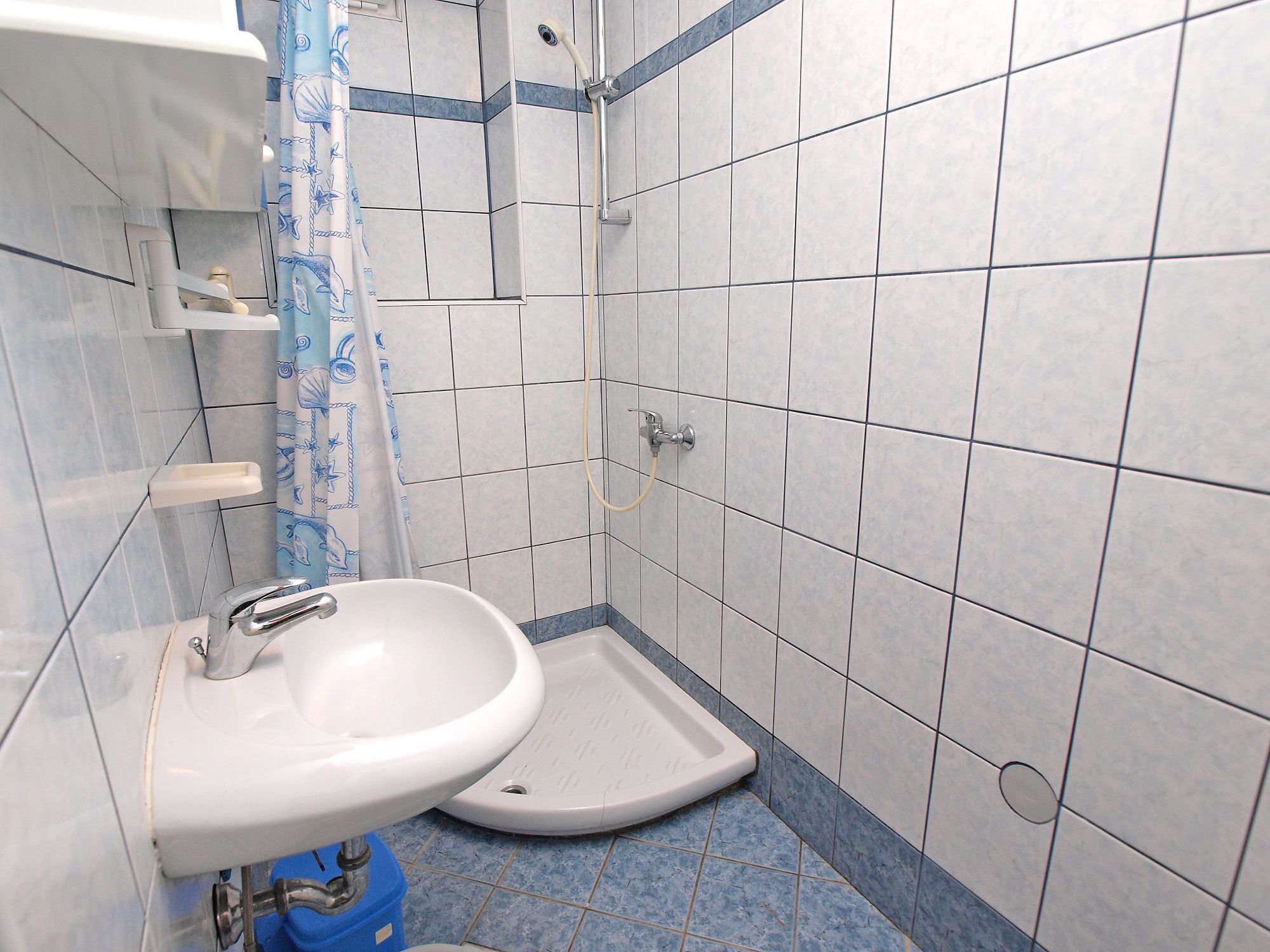 A bathroom with a white sink, a shower, and blue-tiled walls.