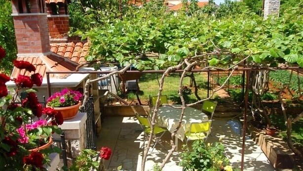 Un jardin agrémenté d’une pergola, d’une structure en briques et d’une terrasse carrelée.
