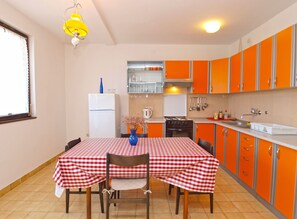 Ett kompakt kök med orange skåp, ett vitt kylskåp och en röd- och vitrutig duk.