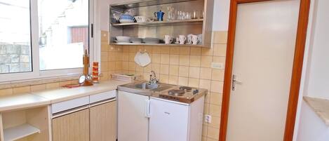 A compact kitchen with a sink, stove, and a small refrigerator. There is a window providing natural light, and a door leading to another room.