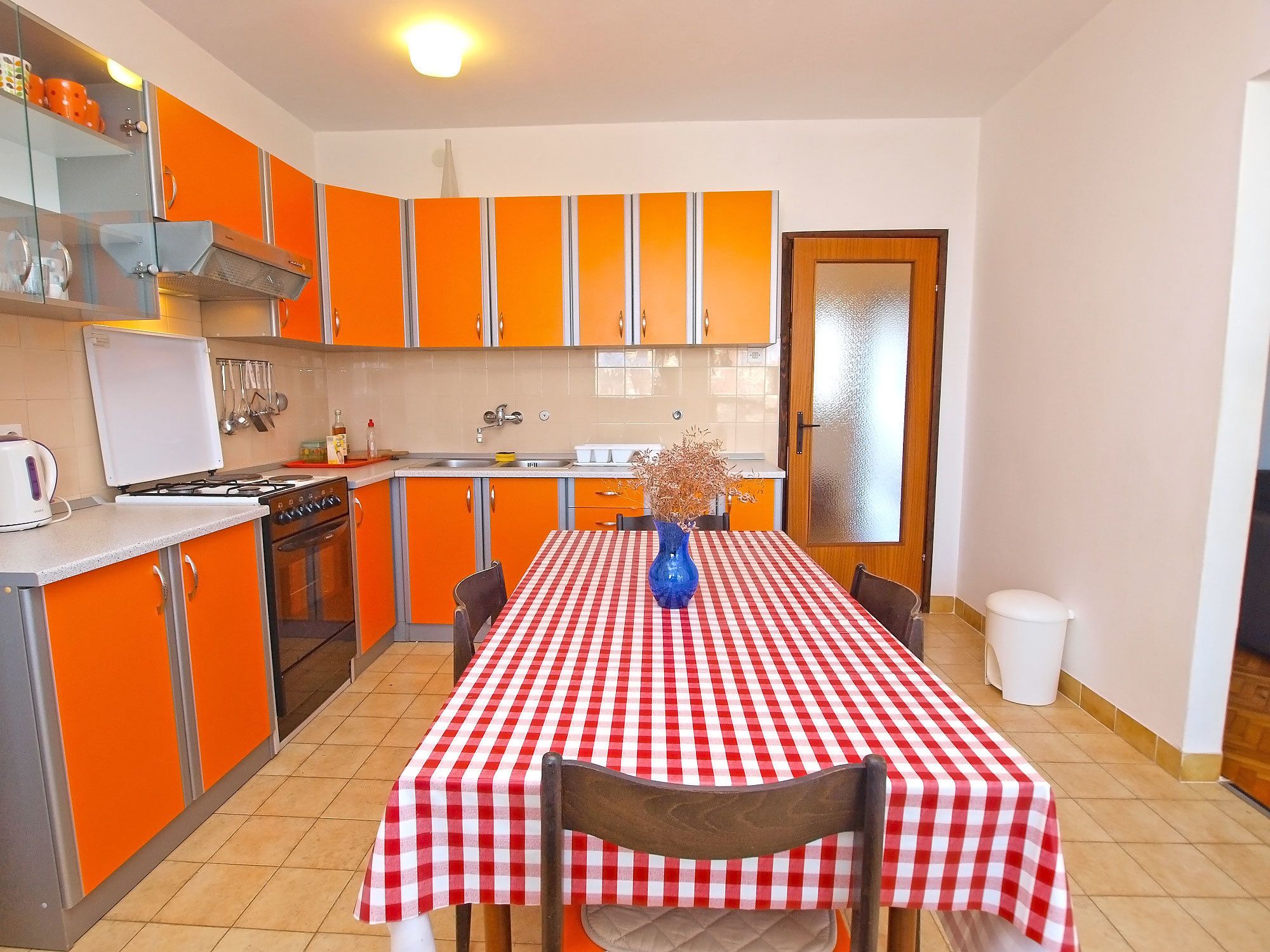 A compact kitchen with orange cabinets, a white stove, and a red and white checkered tablecloth.