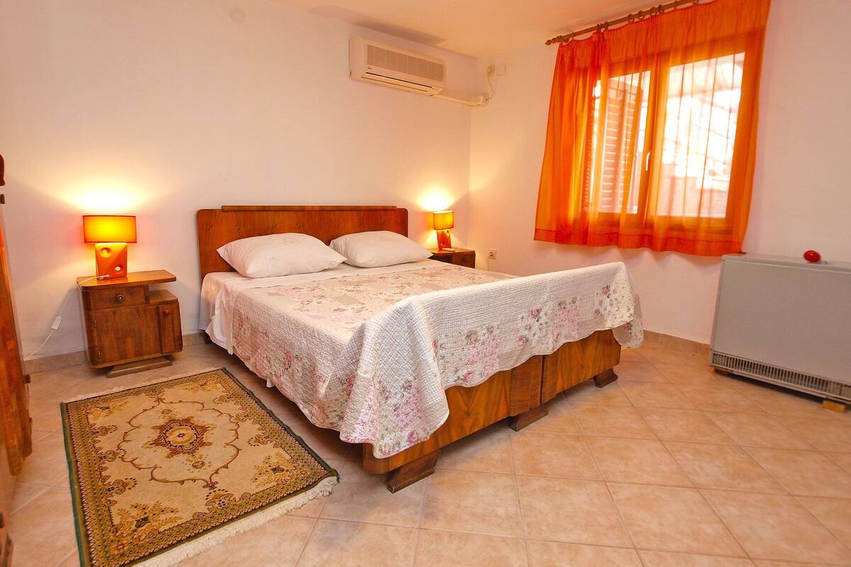 A bedroom with a wooden bed, two bedside lamps, a radiator, and a patterned rug.