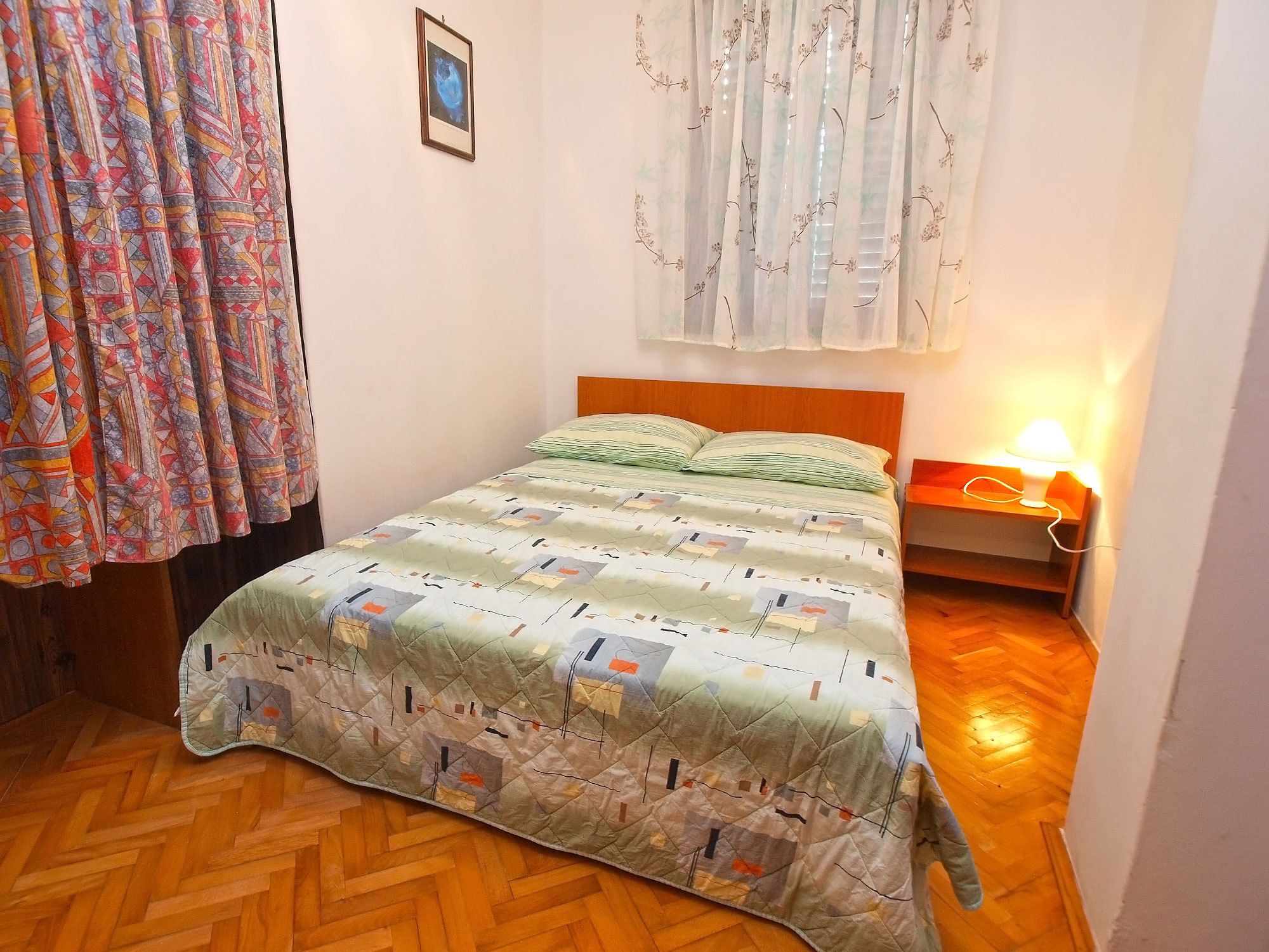 Un dormitorio con una cama de madera, una mesita de noche con lámpara y una colcha estampada.