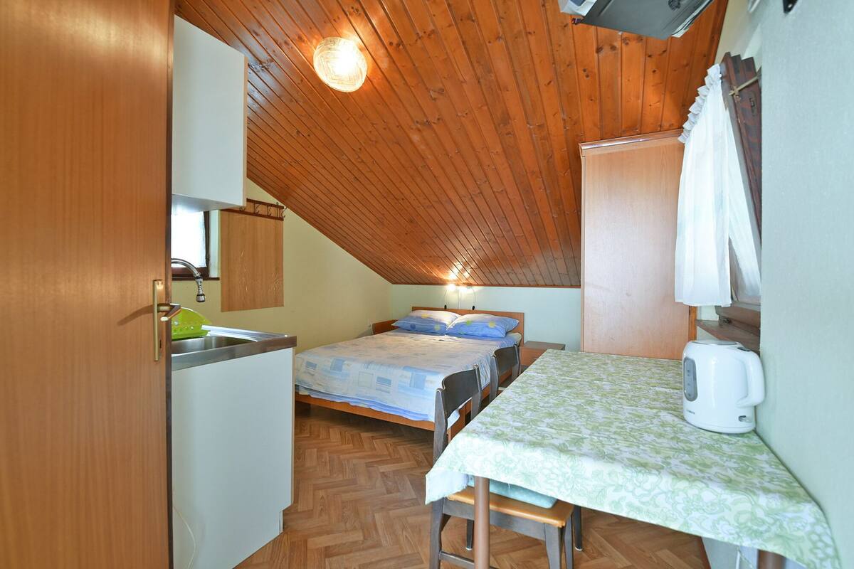 A compact room with a kitchenette, a bed, and a table with a kettle.
