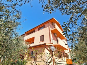A two-story building with a balcony on the upper floor, surrounded by trees.