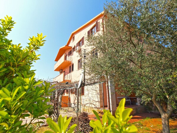 A multi-story building with balconies, surrounded by trees and a garden area.