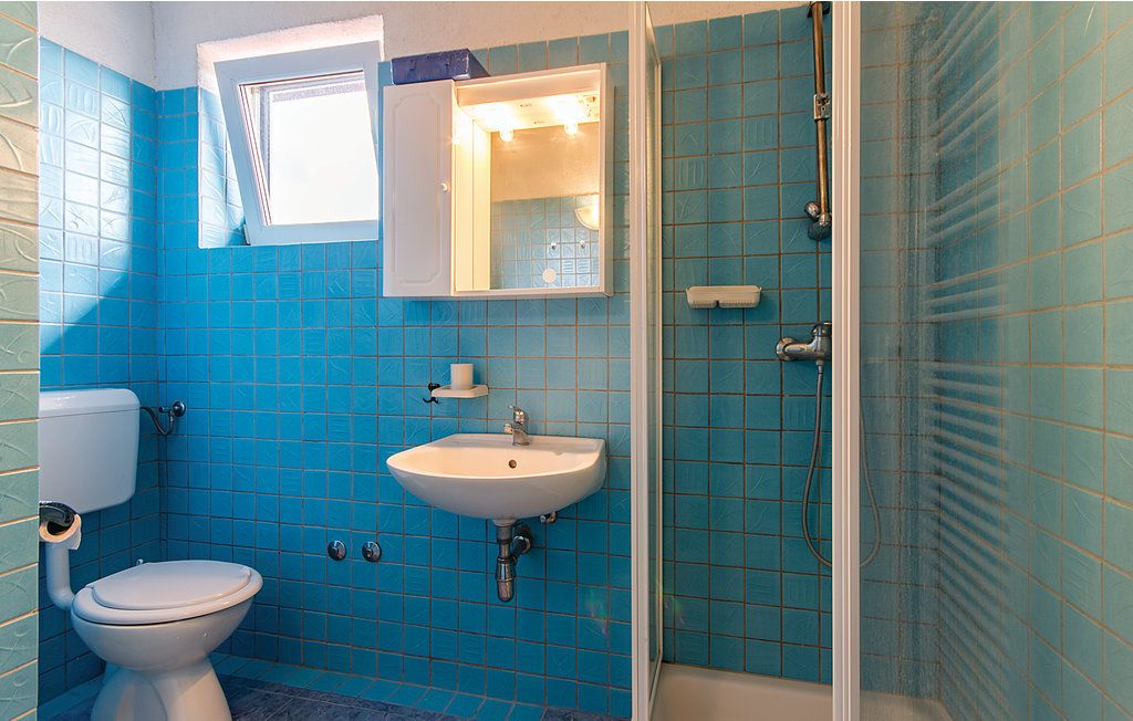 A bathroom with blue tiles, a white sink, a toilet, and a shower enclosure.