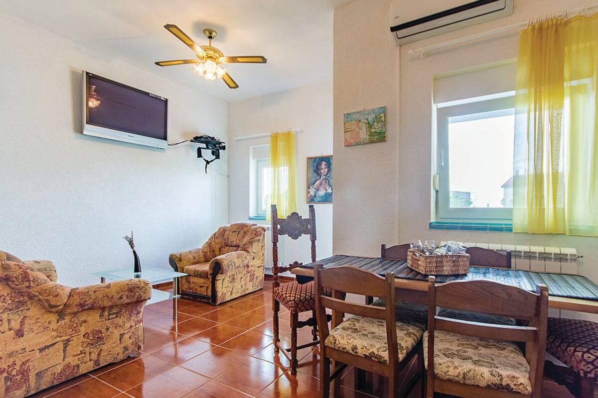A living room with a TV, ceiling fan, dining table, and patterned sofas.