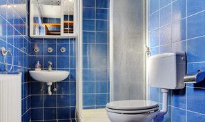 Kylpyhuoneessa on siniset laatat, valkoinen pesuallas, wc ja suihkutila.