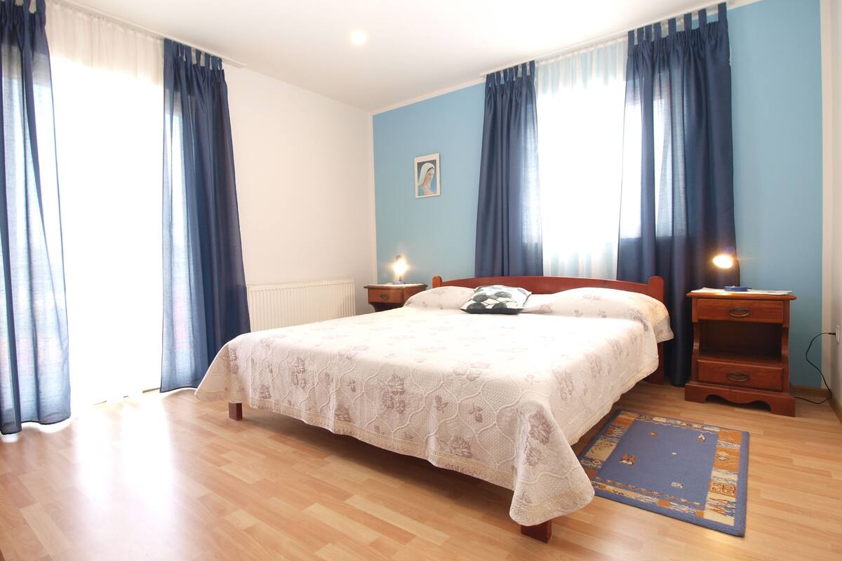 Une chambre avec un grand lit, deux tables de chevet avec des lampes, un mur bleu et un plancher en bois.