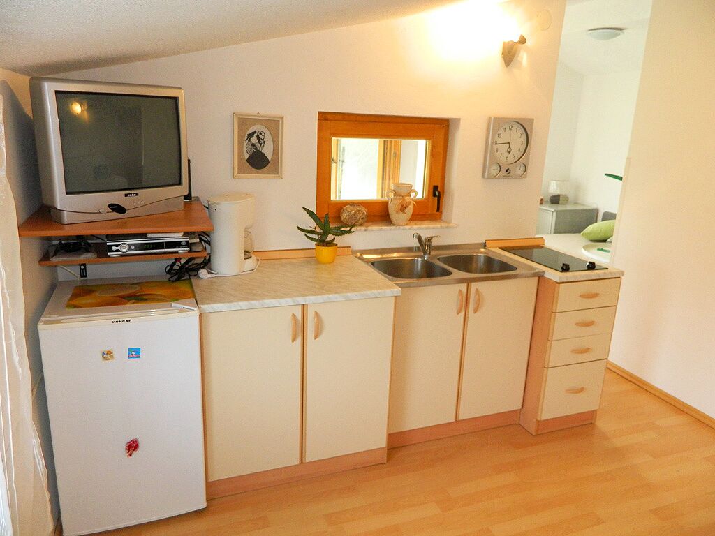 A compact kitchen with a refrigerator, a microwave, a sink, and a window with a mirror above it.