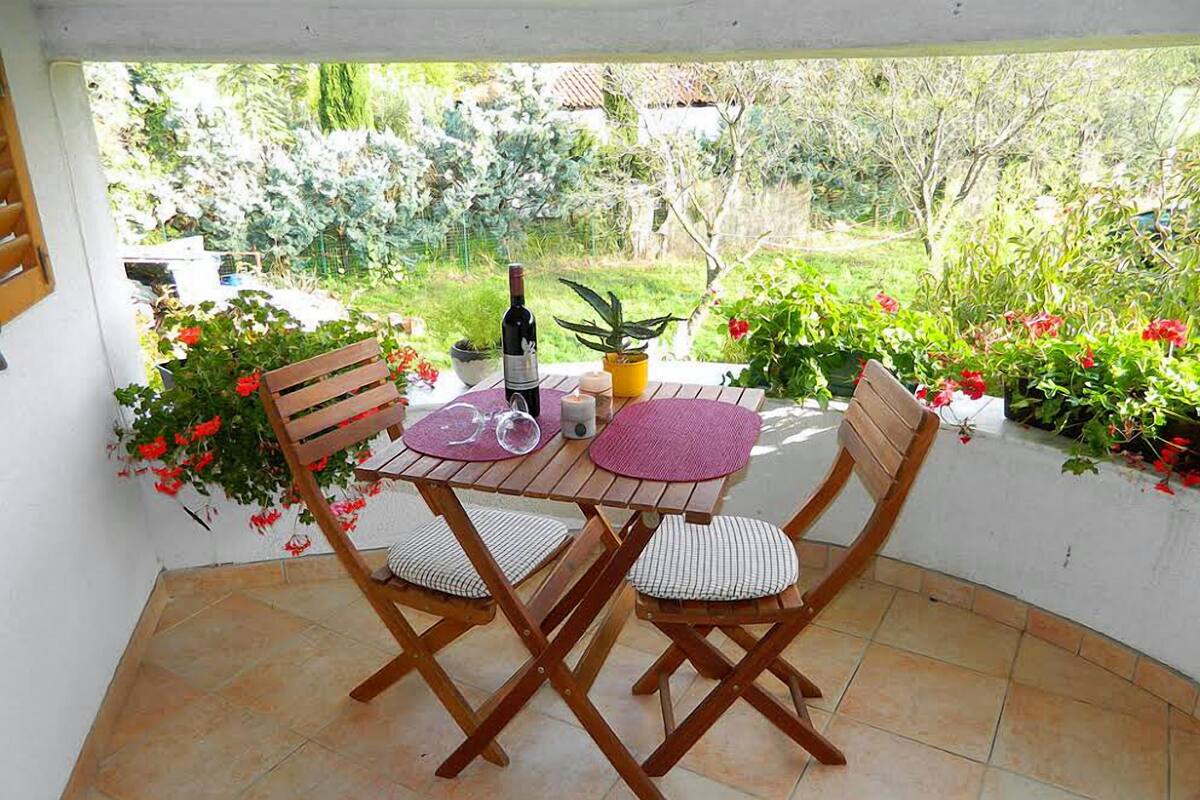 Une terrasse avec une table et des chaises en bois, une bouteille de vin et une bougie.