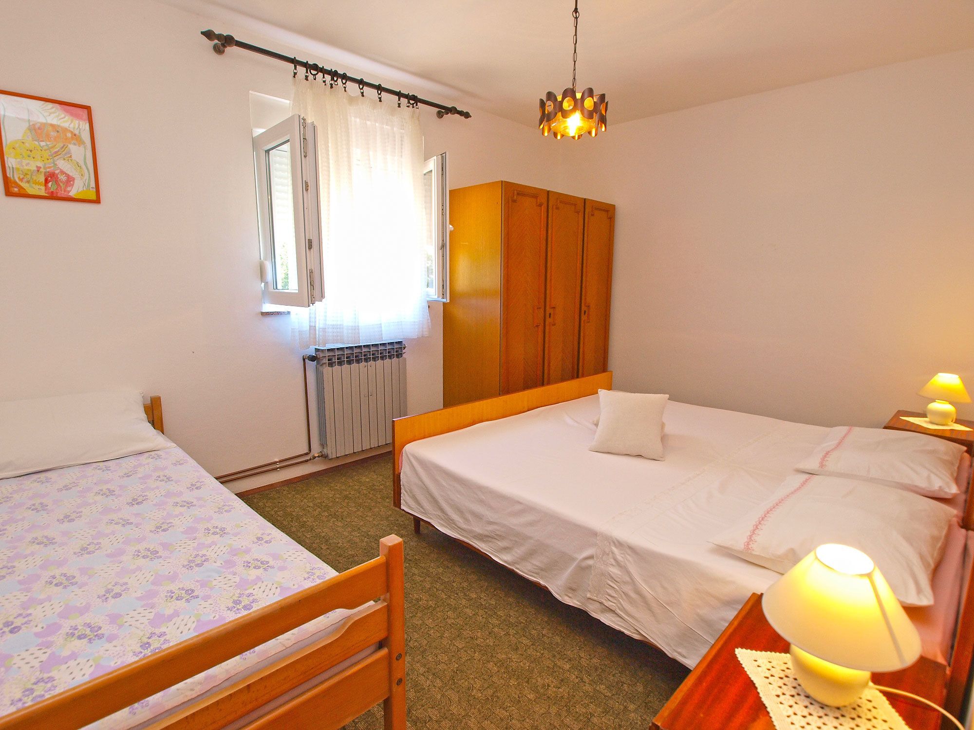 Une chambre avec deux lits, une armoire en bois, un radiateur et une fenêtre avec des rideaux.