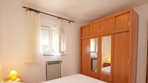 A bedroom with a bed, a wooden wardrobe, a window with curtains, a radiator, and a bedside lamp. - Apartments Marina 947 (Fazana)