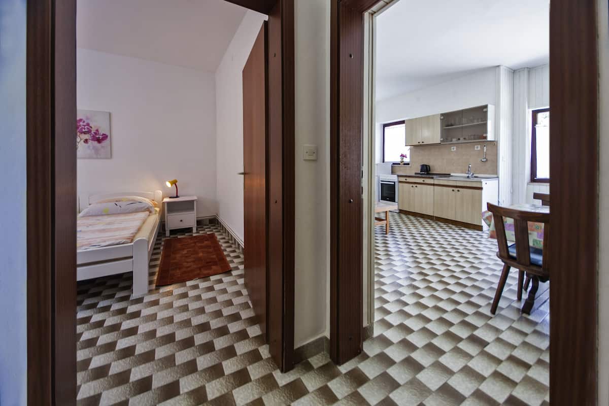 Un dormitorio con suelo a cuadros, una cama, una mesita de noche y una mesilla con una lámpara.