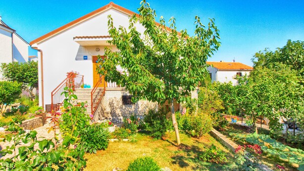 Una villa blanca con techo de tejas rojas, rodeada de exuberantes jardines y un cielo azul despejado.