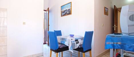A dining area with a table set for two, chairs, a small table with a bowl, and a painting on the wall.