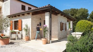 A stone building with a tiled roof, potted plants, and a person carrying a tray. - Apartments Valter 881 (Novigrad)