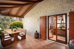 An outdoor patio area with a wooden table and benches, a stone wall, and a sliding glass door leading to an interior space with a bookshelf and a dining table. - Apartments Valter 881 (Novigrad)