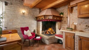 A rustic kitchen with a stone fireplace, wooden beams, and a dining area with a red chair and table. - Apartments Valter 881 (Novigrad)