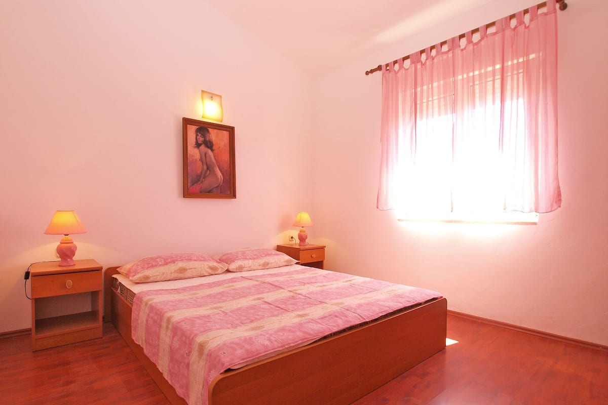A bedroom with a wooden bed, two bedside lamps, a painting on the wall, and a window with curtains.