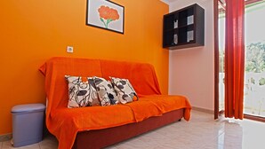 Een kamer met een oranje bank, een lijst met een bloem, een zwart plank en een blauwe prullenbak.