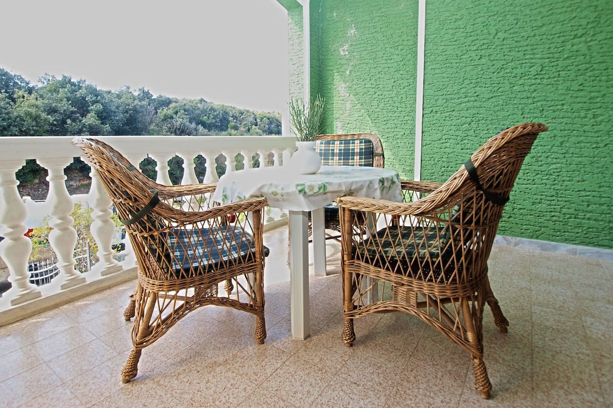 Un balcon avec des fauteuils en osier et une table, des murs verts et une vue sur les arbres.
