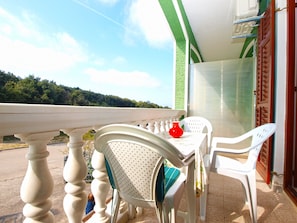 A balcony with a table and chairs, a red vase, and a view of a green landscape.