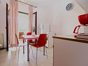 A dining area with a red and white checkered tablecloth, red chairs, and a white refrigerator in the background.