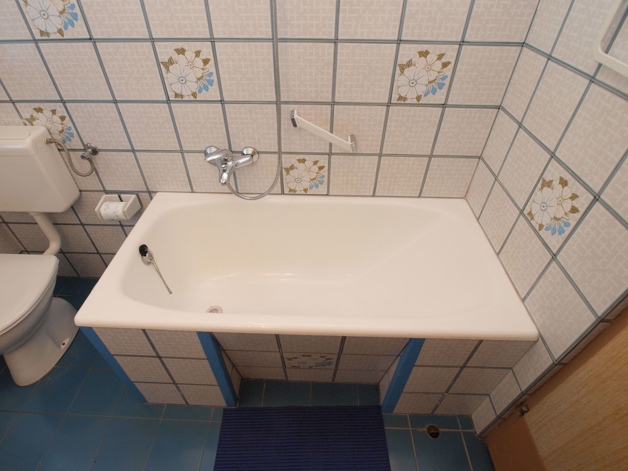 A bathroom with a white bathtub, a toilet, and a blue floor.