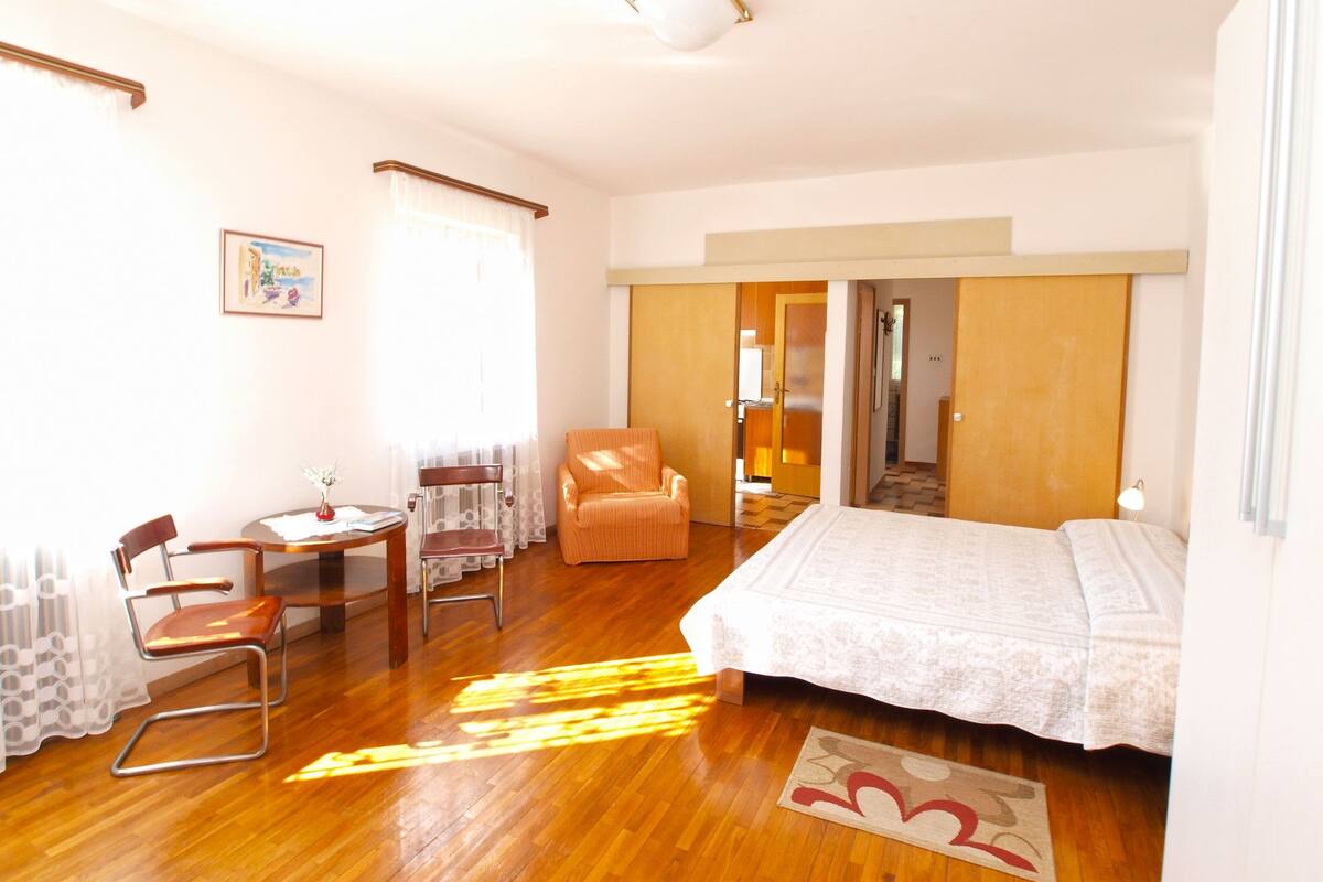 Habitación de hotel con una cama, una silla, una mesita y un escritorio. Se ve una puerta que da a otra habitación.