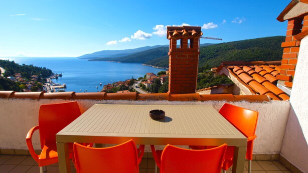 A terrace with a table and chairs, overlooking a coastal view with a clear sky. - Apartments Marisa 981 (Labin)